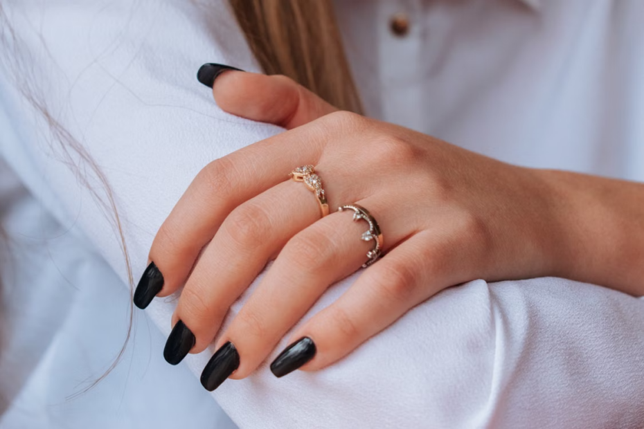 imagem da mão de uma pessoal com as unhas feitas e anéis dourados em destaque