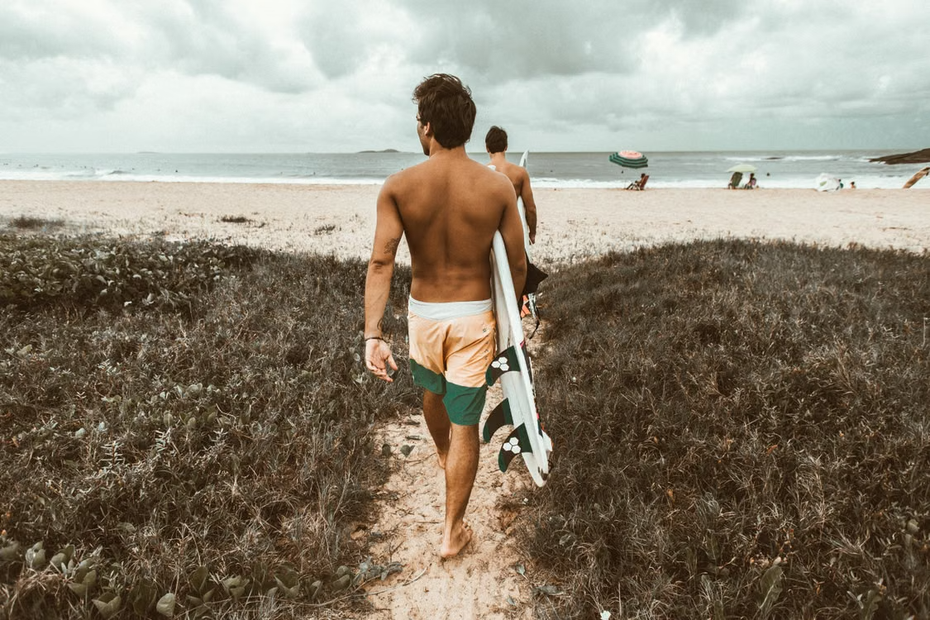 homem com prancha de surf caminhando na praia